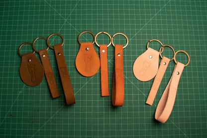 An array of keychains organized by color. A round, flat, and loop keychain in brown, light brown, and natural leather color.