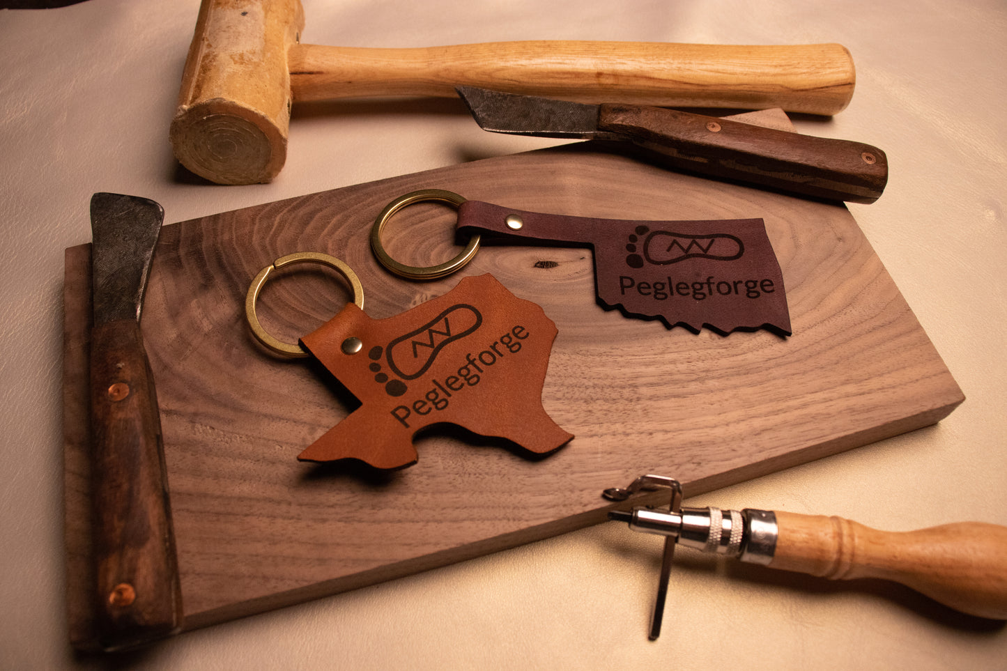 Texas and Oklahoma shaped keychains surrounded by leather working tools.