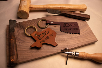 Texas and Oklahoma shaped keychains surrounded by leather working tools.