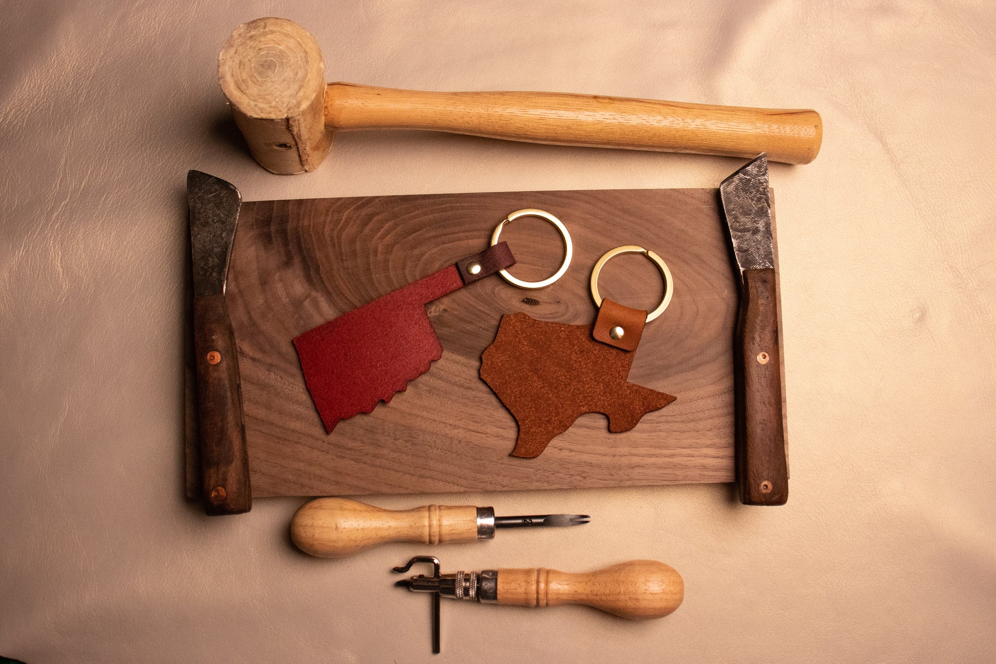 Backside of Texas and Oklahoma shaped keychains surrounded by leather working tools.