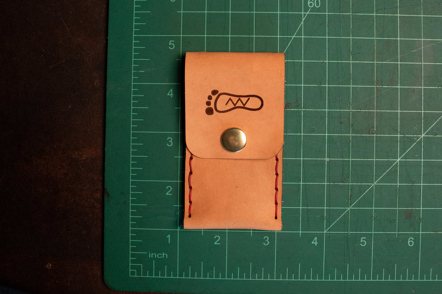 Natural vegetable tanned leather sewn thumb drive necklace on measuring table. It measures 2 inch long and 3.5 inches tall.