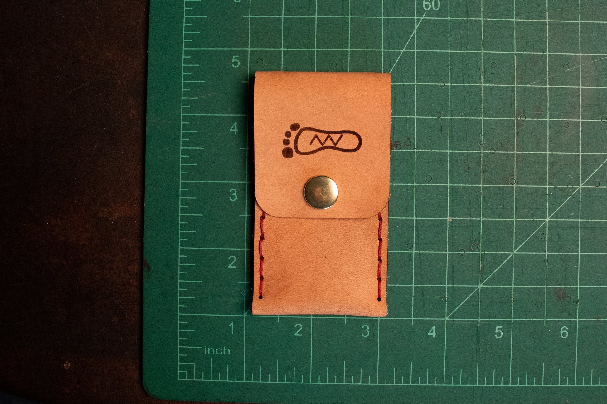 Natural vegetable tanned leather sewn thumb drive necklace on measuring table. It measures 2 inch long and 3.5 inches tall.